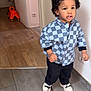 Sacha participe au concours pour gagner de l'argent avec cette photo : child, curly_hair, checkered_shirt, black_pants, white_shoes, indoor, tiled_floor, wooden_floor, doorway, toy, orange_toy, walking, young_child, curious_expression, home_interior, person, floor, casual_clothing, standing, young_kid