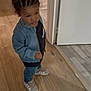 child, toddler, denim_jacket, braided_hair, sneakers, wooden_floor, indoor, standing, serious_expression, person, casual_clothing, doorway, floor_transition, young_child, hair_style, footwear, home, small_person, curious, determined