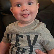 Luke is registered to the contest to win money with this photo: baby, child, tongue_out, gray_shirt, shorts, indoor, couch, person, smiling, cute, infant, cheeky, happy, seated, human, young_child, casual_clothing, room, portrait, skin