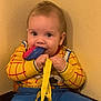 baby, child, indoor, toy, yellow, blue, clothing, wall, sitting, playful, curious, lanyard, face, person, young_child, colorful, chewing, woodysuit, cute, infant