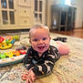 Luke is registered to the contest to win money with this photo: baby, smiling, carpet, toy, indoor, child, playtime, furniture, colorful, patterned_rug, happy, person, floor, crawling, long_sleeve_shirt, home, cute, infant, bright, cozy