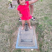 Joelee joined the competition — help win amazing prizes! child, girl, barefoot, red_dress, flowers, grave, gravestone, grass, outdoor, smiling, person, adult, holding, memorial, headstone, cemetery, nature, happy, casual_clothing, supporting_hand