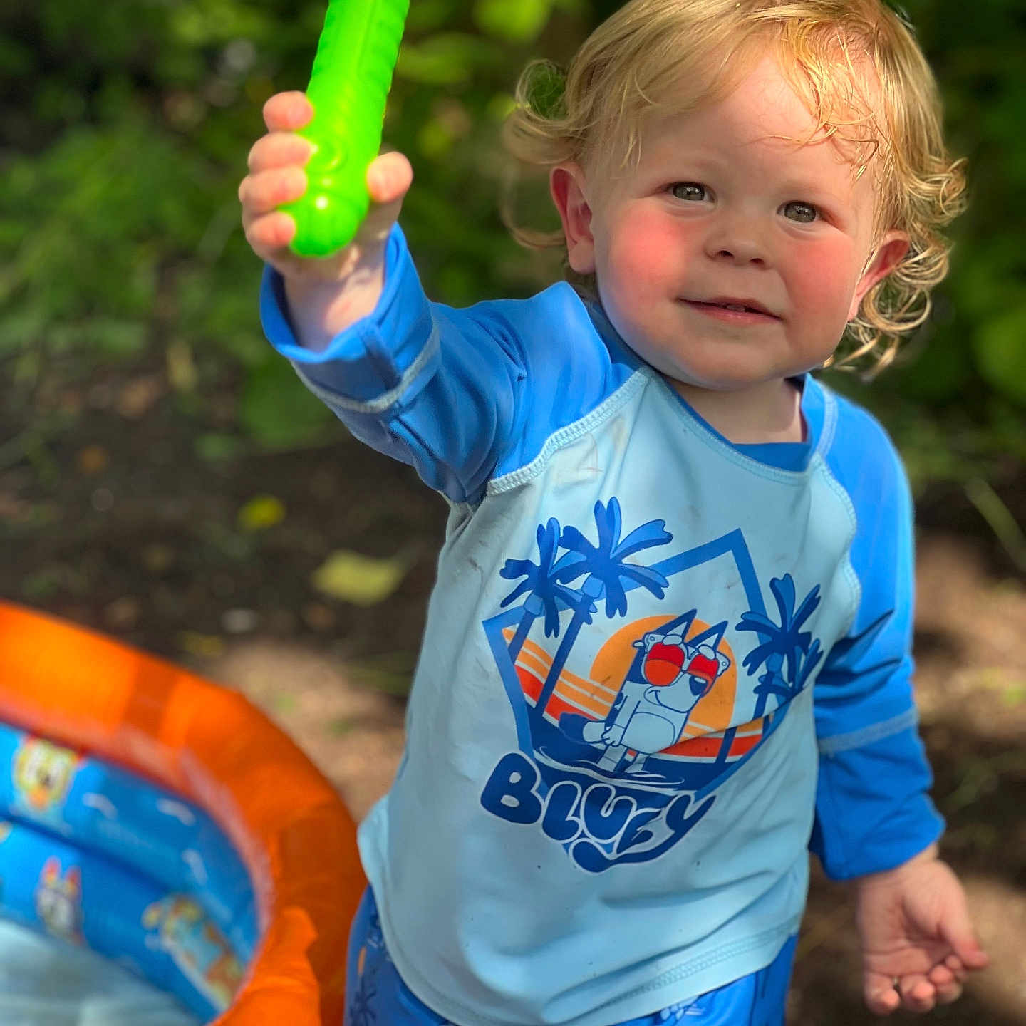Waylon joined the competition — help win amazing prizes! blonde_hair, blue_shirt, blue_shorts, bluey, child, curly_hair, fun, green_toy, inflatable_pool, nature, outdoor, person, play, rosy_cheeks, smiling, summer, sunlight, toddler, toy, water_toy