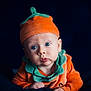 baby, infant, child, pumpkin_costume, orange_hat, blue_eyes, cute, portrait, costume, soft_lighting, dark_background, curious_expression, hands, face, headwear, fall_theme, seasonal, closeup, clothing, adorable