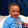 baby, child, smiling, blue_shirt, cartoon_print, bed, headboard, indoor, happy, sitting, person, portrait, cute, infant, clothing, baby_boy, young_child, face, skin, hair