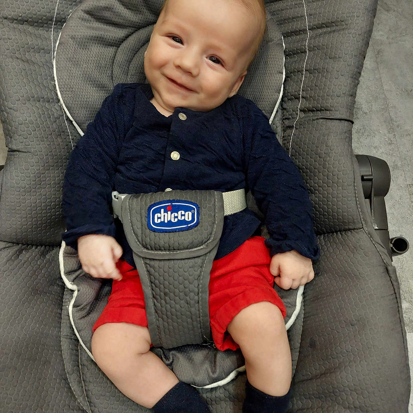 Jules a rejoint le concours — aidez-le/la à gagner de superbes lots ! baby, baby_chair, chicco, child, clothing, comfort, cute, face, floor, happy, indoor, infant, navy_top, padded_seat, person, portrait, red_shorts, seatbelt, smiling, socks