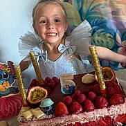 Evy a rejoint le concours — aidez-le/la à gagner de superbes lots ! child, girl, birthday_cake, strawberries, raspberries, number_candle, sparkly_dress, party, celebration, smiling, happy, fruit, dessert, table, colorful_background, tulle_bow, pastry, food, indoors, festive