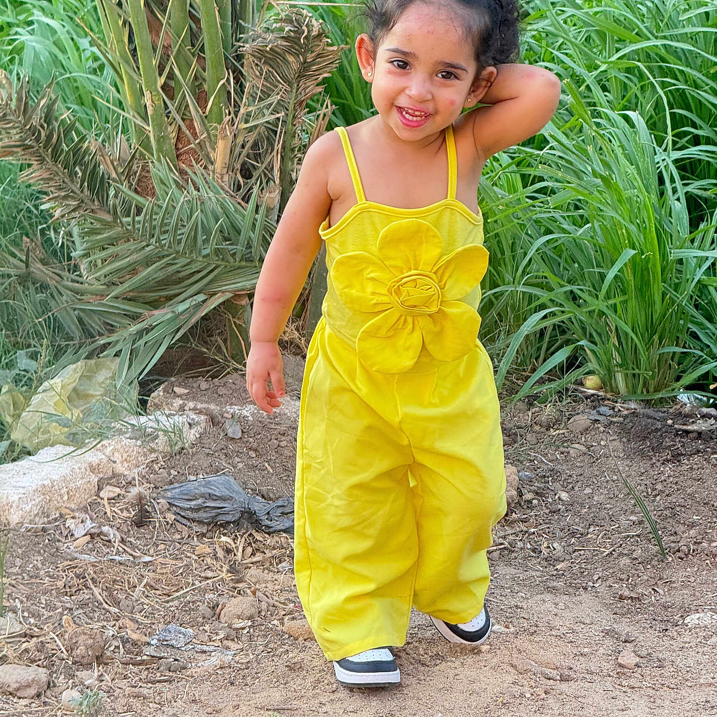 Clara Ferjallah joined the competition — help win amazing prizes! casual, casual_shoes, child, curly_hair, cute, dirt_path, flower, girl, greenery, happy, nature, outdoor, plants, playful, portrait, smile, sunlight, walking, yellow_outfit, young_child