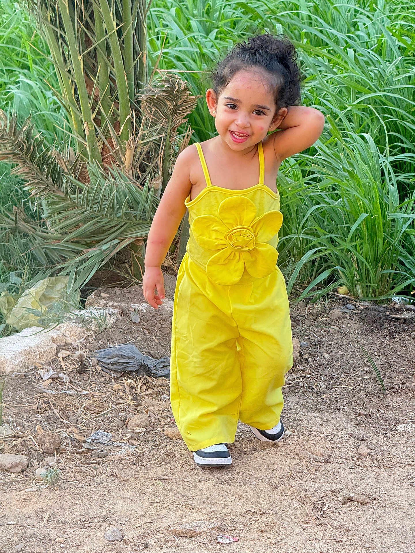 Clara Ferjallah joined the competition — help win amazing prizes! casual, casual_shoes, child, curly_hair, cute, dirt_path, flower, girl, greenery, happy, nature, outdoor, plants, playful, portrait, smile, sunlight, walking, yellow_outfit, young_child