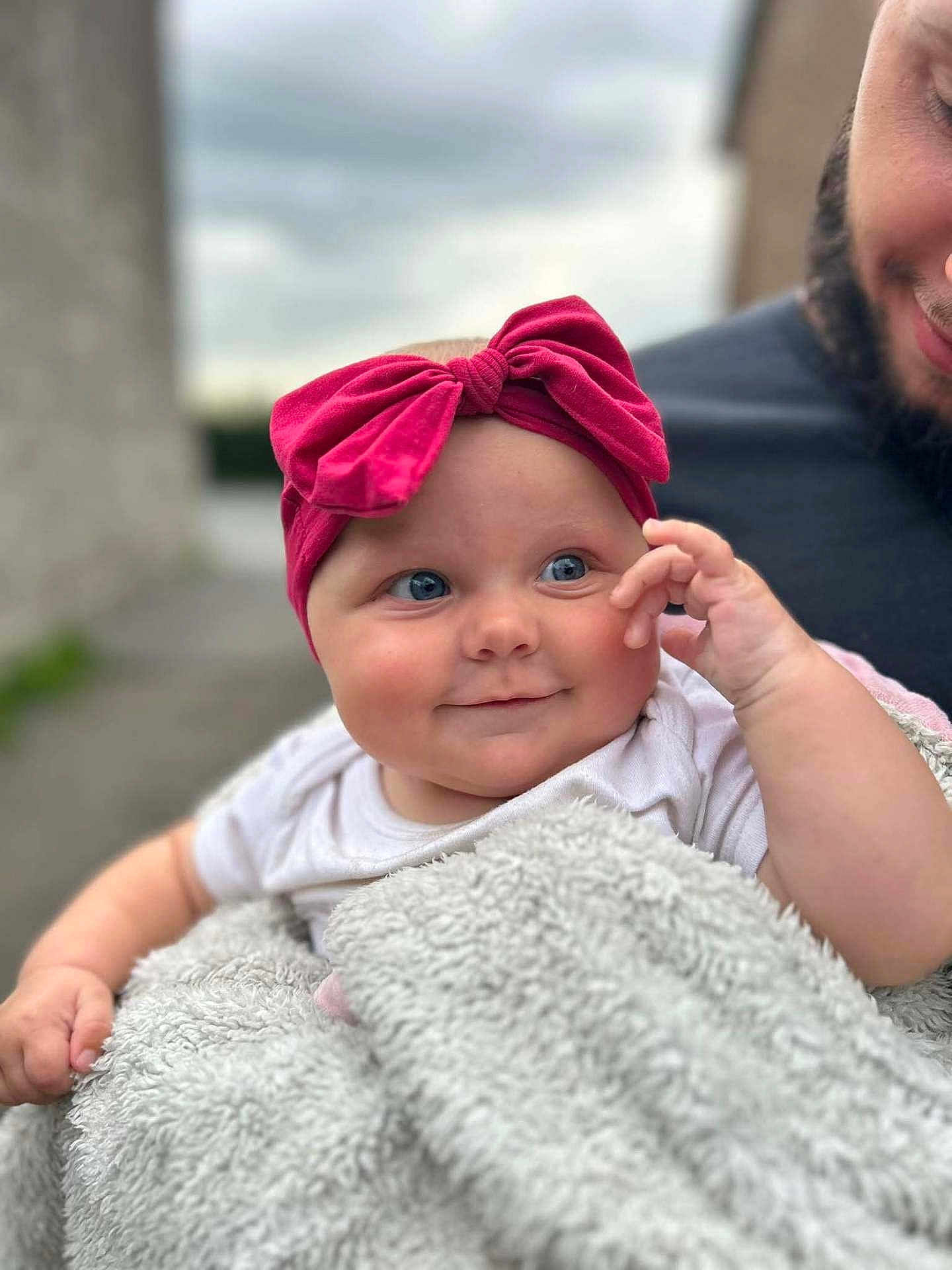 Leya participe au concours pour gagner de l'argent avec cette photo : baby, child, smile, blue_eyes, pink_bow, blanket, fluffy, person, adult, beard, outdoor, portrait, cute, happy, holding, face, headwear, clothing, infant, expression