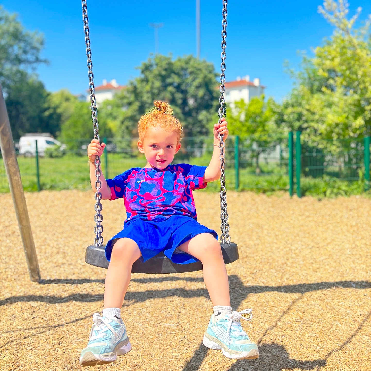 Noyan-Latif a rejoint le concours — aidez-le/la à gagner de superbes lots ! child, swing, playground, outdoor, sunny, blue_sky, trees, greenery, woodchips, shadow, red_hair, curly_hair, holding_chains, sneakers, shorts, tshirt, happy, smiling, daytime, recreation