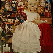 Aubree joined the competition — help win amazing prizes! toddler, child, girl, white_dress, pink_boots, lollipop, toy, teddy_bear, christmas, holiday, decorations, indoor, festive, cute, portrait, smiling, ribbons, bows, gift_box, wooden_shelf