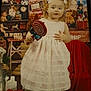 toddler, child, girl, white_dress, pink_boots, lollipop, toy, teddy_bear, christmas, holiday, decorations, indoor, festive, cute, portrait, smiling, ribbons, bows, gift_box, wooden_shelf
