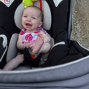 Lorelai is registered to the contest to win money with this photo: baby, car_seat, smiling, happy, infant, foot, plush_toy, ladybug, outdoor, gravel, child, seat_belt, clothing, person, cute, head, sitting, playful, toy, bright