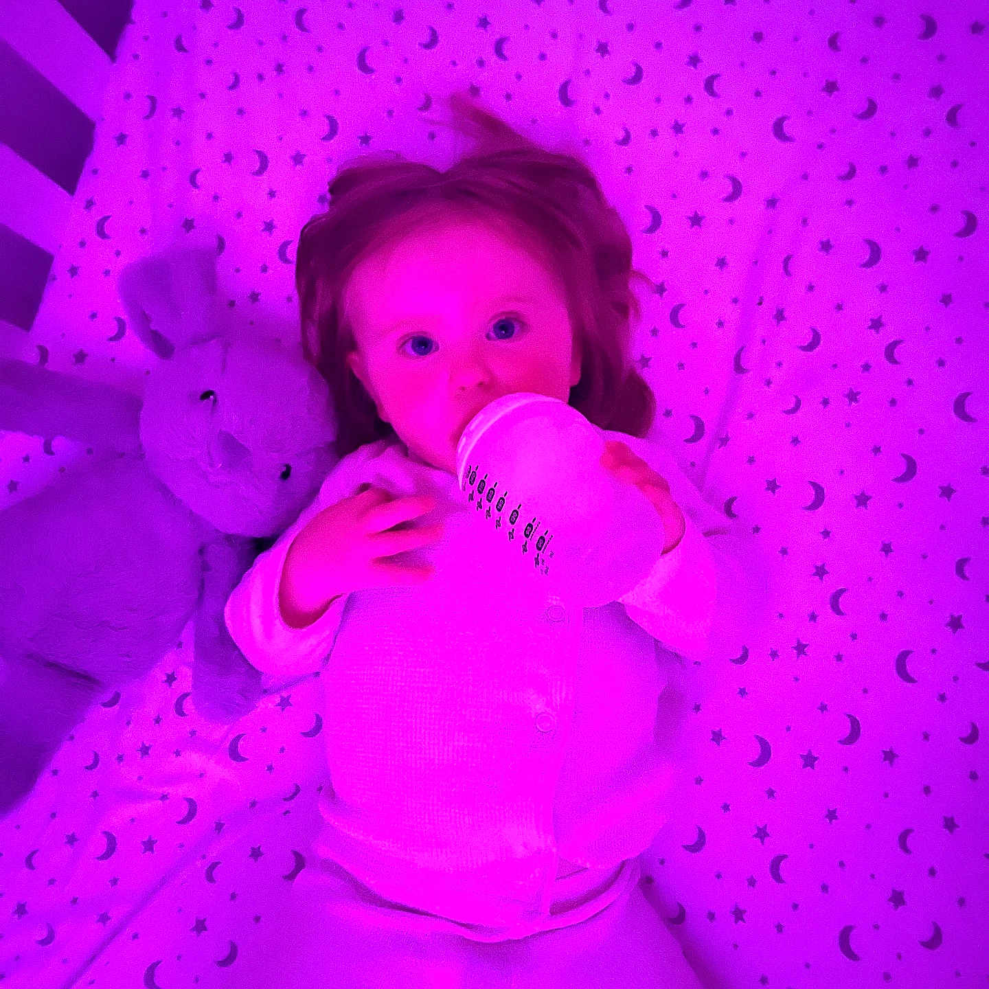 Eliana-Rose is registered to the contest to win money with this photo: baby, blue_eyes, bottle, child, cozy, crib, cute, feeding, indoor, infant, lying_down, moon, pattern, plush_bunny, purple_lighting, sheet, sleepwear, sleepy, stars, toy