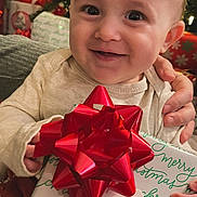 Preston is registered to the contest to win money with this photo: baby, child, smiling, present, gift, red_bow, christmas, holiday, tree, decorations, indoor, cute, happy, person, festive, celebration, wrapped_gift, hand, tag, cozy