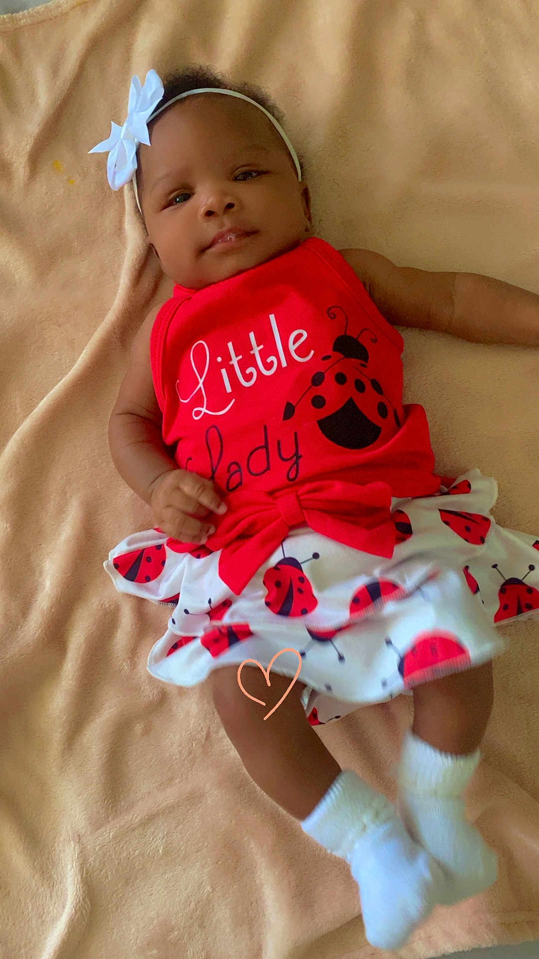 Nyla is registered to the contest to win money with this photo: baby, infant, child, red_clothing, headband, bow, blanket, ladybug_pattern, skirt, white_socks, cute, smiling, lying_down, soft_texture, portrait, indoors, happy, young_child, fashion, accessory