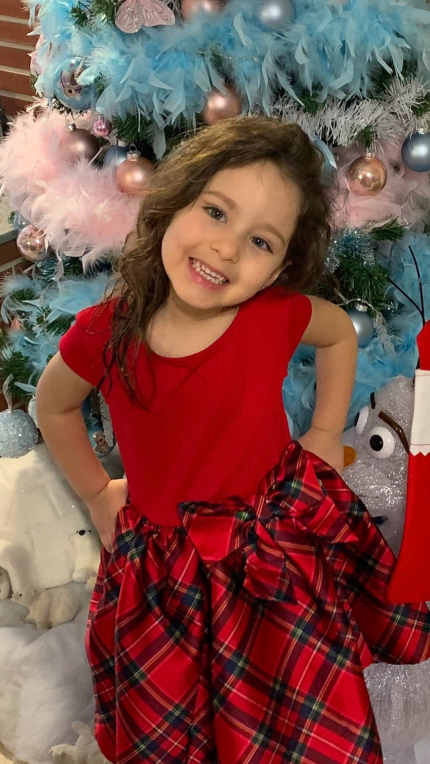 Carla a rejoint le concours — aidez-le/la à gagner de superbes lots ! baby_toddler_clothing, blue, christmas_ornament, christmas_tree, day_dress, dress, facial_expression, fashion, green, hairstyle, happy, holiday_ornament, joy, person, pink, plaid, smile, tartan, textile, toddler