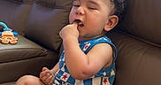 Kobe is registered to the contest to win money with this photo: toddler, child, indoor, couch, blanket, blue_clothing, socks, curly_hair, finger_in_mouth, sleepy, window_light, leather_couch, toy, patterned_blanket, casual, seated, home, relaxed, portrait, baby