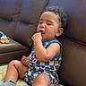 toddler, child, indoor, couch, blanket, blue_clothing, socks, curly_hair, finger_in_mouth, sleepy, window_light, leather_couch, toy, patterned_blanket, casual, seated, home, relaxed, portrait, baby