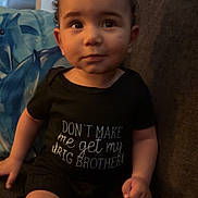 Kobe is registered to the contest to win money with this photo: toddler, child, baby, curly_hair, black_onesie, couch, indoor, home, furniture, sitting, cute, expression, face, person, clothing, legs, funny_text, living_room, cozy, young_child