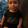 toddler, child, baby, curly_hair, black_onesie, couch, indoor, home, furniture, sitting, cute, expression, face, person, clothing, legs, funny_text, living_room, cozy, young_child