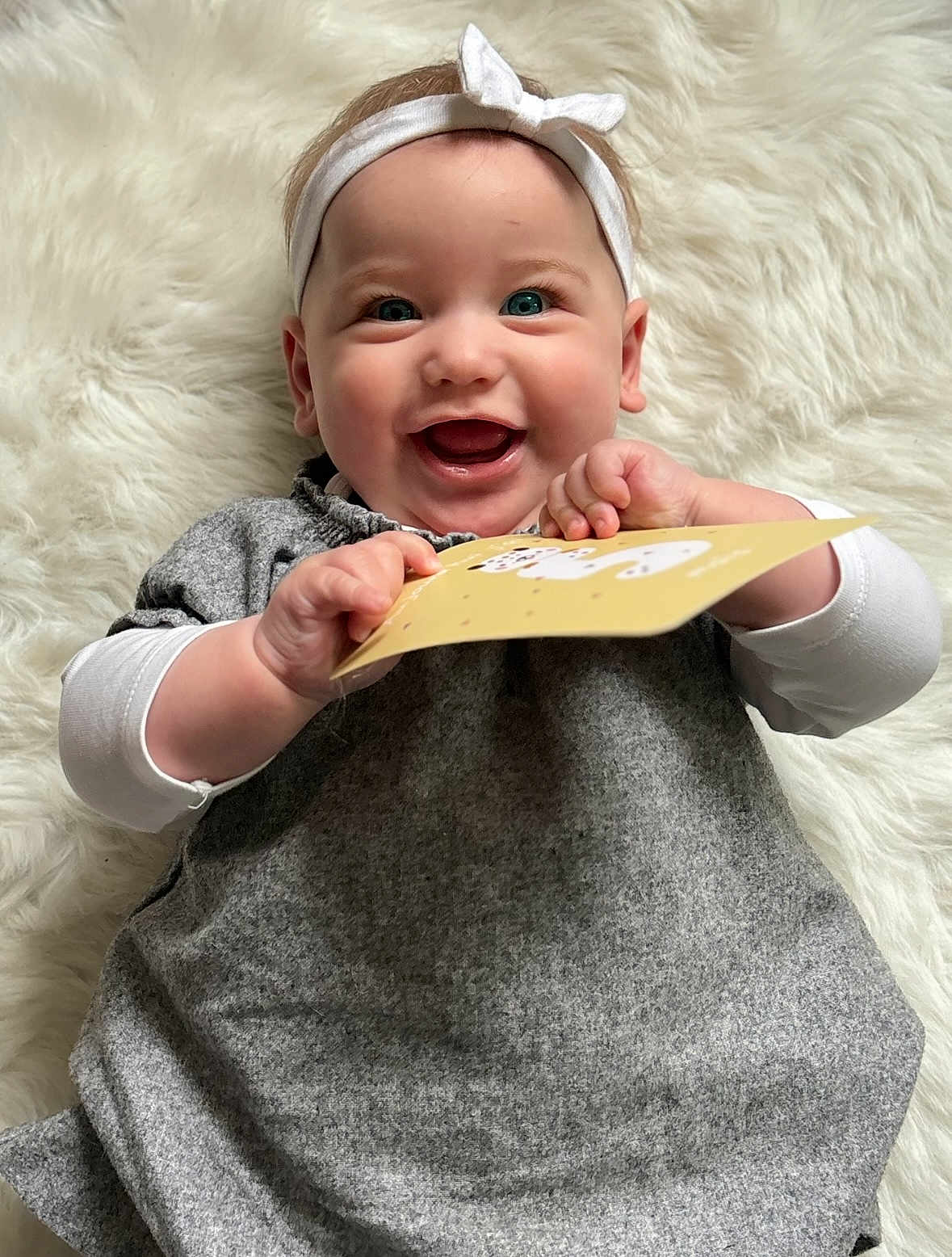 Bianca a rejoint le concours — aidez-le/la à gagner de superbes lots ! baby, blue_eyes, card, child, closeup, cute, fluffy_background, gray_dress, hands, happy, headband, indoor, infant, joyful, lying_down, person, playful, portrait, smile, white_sleeves