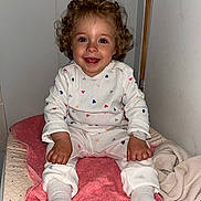 Charlotte participe au concours pour gagner de l'argent avec cette photo : toddler, child, curly_hair, blue_eyes, white_outfit, hearts_pattern, pink_towel, sitting, indoors, smiling, happy, cozy, blanket, clothing, person, portrait, cute, baby, feet, hands