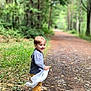casual, child, clothing, daylight, dirt_path, forest, greenery, happy, leaves, nature, outdoor, path, playful, smiling, sneakers, toddler, trees, walking, white_cloth, young_child