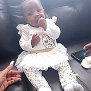 D'Aruia joined the competition — help win amazing prizes! baby, infant, child, sitting, couch, black_leather, white_clothing, tutu, patterned_pants, bow, hand, smartphone, indoor, cute, young_child, portrait, support, curious, fingers, footwear