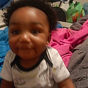 Nishan is registered to the contest to win money with this photo: baby, child, indoor, blanket, clothing, bed, person, infant, smile, hair, toddler, cute, furniture, room, home, fabric, pink_blanket, gray_blanket, blue_cloth, playful