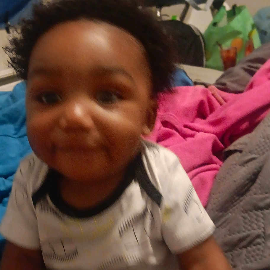 Nishan is registered to the contest to win money with this photo: baby, child, indoor, blanket, clothing, bed, person, infant, smile, hair, toddler, cute, furniture, room, home, fabric, pink_blanket, gray_blanket, blue_cloth, playful