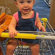 Aliviah joined the competition — help win amazing prizes! child, toddler, shopping_cart, denim_overalls, pink_bow, pink_shoes, retail_store, aisle, blue_floor, hand, smile, face, person, clothing, bag, yellow_handle, indoor, cute, baby, footwear