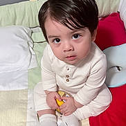 Eduardo joined the competition — help win amazing prizes! toddler, child, baby, indoor, quilt, pillow, blanket, socks, white_clothing, curly_hair, cute, sitting, holding_object, soft_lighting, looking_up, bed, home, face, young, innocent
