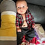Malakai is registered to the contest to win money with this photo: baby, infant, couch, pillow, plaid_shirt, barefoot, blanket, red, black, gray, face, head, skin, hand, foot, indoors, seated, clothing, expressionless, holiday