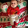 baby, infant, smile, red_clothing, white_pants, christmas_blanket, holiday_theme, socks, santa, face, person, cozy, indoor, carpet, festive, cute, child, happy, couch, blanket
