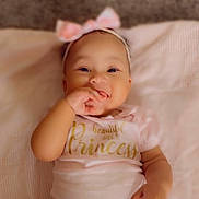 Kailey is registered to the contest to win money with this photo: baby, blanket, child, cute, fingers, hand, happy, headband, indoors, infant, lying_down, person, pink_bow, portrait, princess, shirt, smiling, soft, text, young