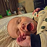 newborn, baby, infant, sleepy, yawning, face, portrait, bed, blanket, swaddled, hand, fingers, indoors, bedroom, cozy, patterned_blanket, lying_down, close_up, family_photo, child