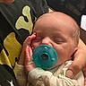newborn, baby, infant, sleeping, pacifier, cuddled, adult, hand, face, portrait, close_up, indoors, family, caregiving, onesie, clothing, soft_lighting, relaxed, tender, photography