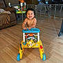 toddler, child, walker_toy, smiling, indoor, living_room, wooden_floor, curly_hair, happy, baby, play_area, furniture, couch, toy, person, flooring, childhood, home, cute, exploring