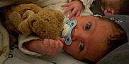 Noah is registered to the contest to win money with this photo: baby, teddy_bear, pacifier, blanket, hand, face, infant, sleepwear, close_up, cute, child, soft_toy, lying_down, indoors, newborn, person, comfort, resting, warm, cozy