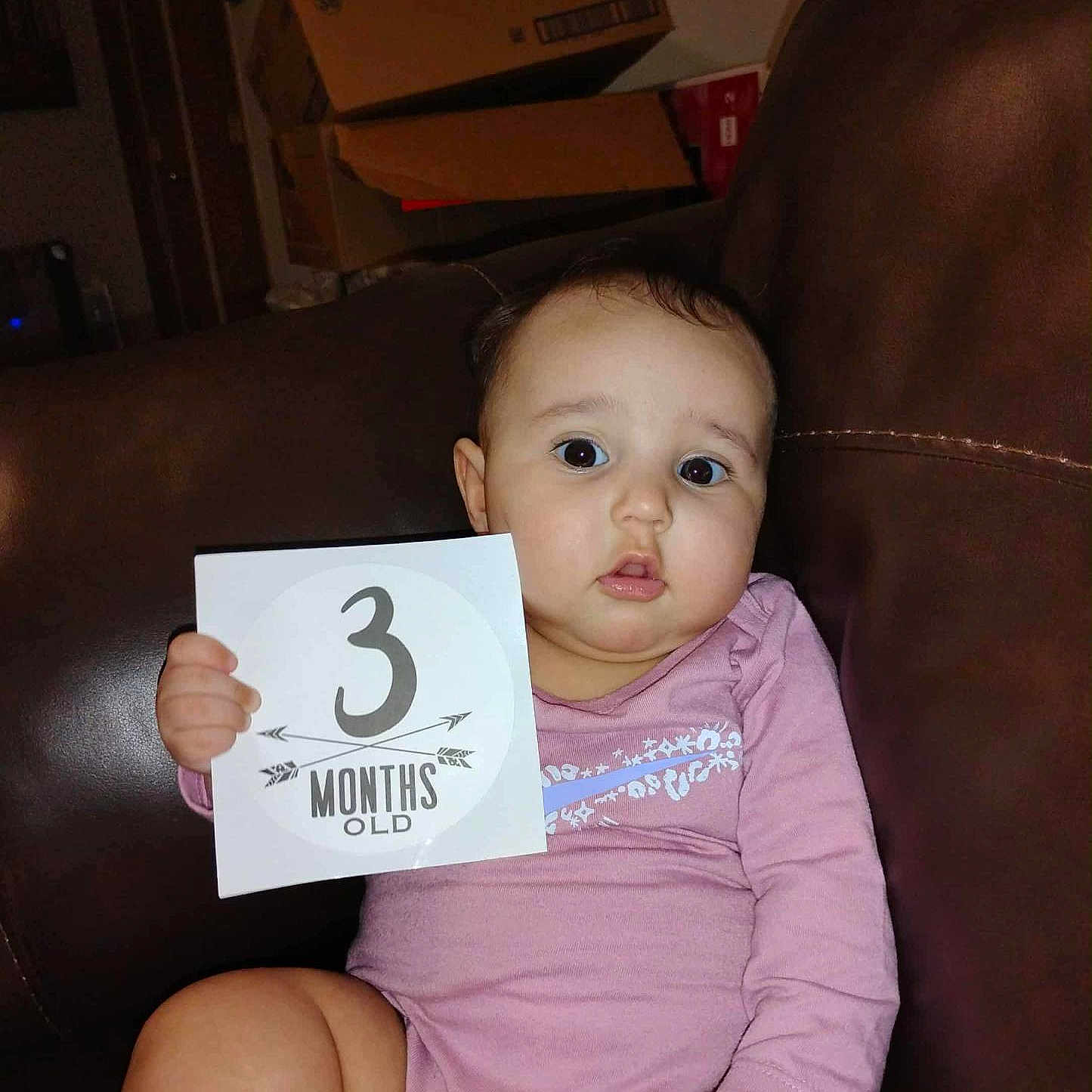 Jesy is registered to the contest to win money with this photo: 3_months_old, baby, cardboard_boxes, casual, child, couch, cute, expression, face, holding, home, indoor, infant, leather, person, pink_clothing, portrait, sign, sitting, young