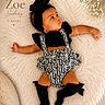 baby, infant, girl, black_headband, flower_headband, black_top, patterned_overalls, knee_high_socks, fluffy_rug, white_rug, lying_down, cute, portrait, flowers, decor, soft_texture, newborn, child, adorable, studio_photo