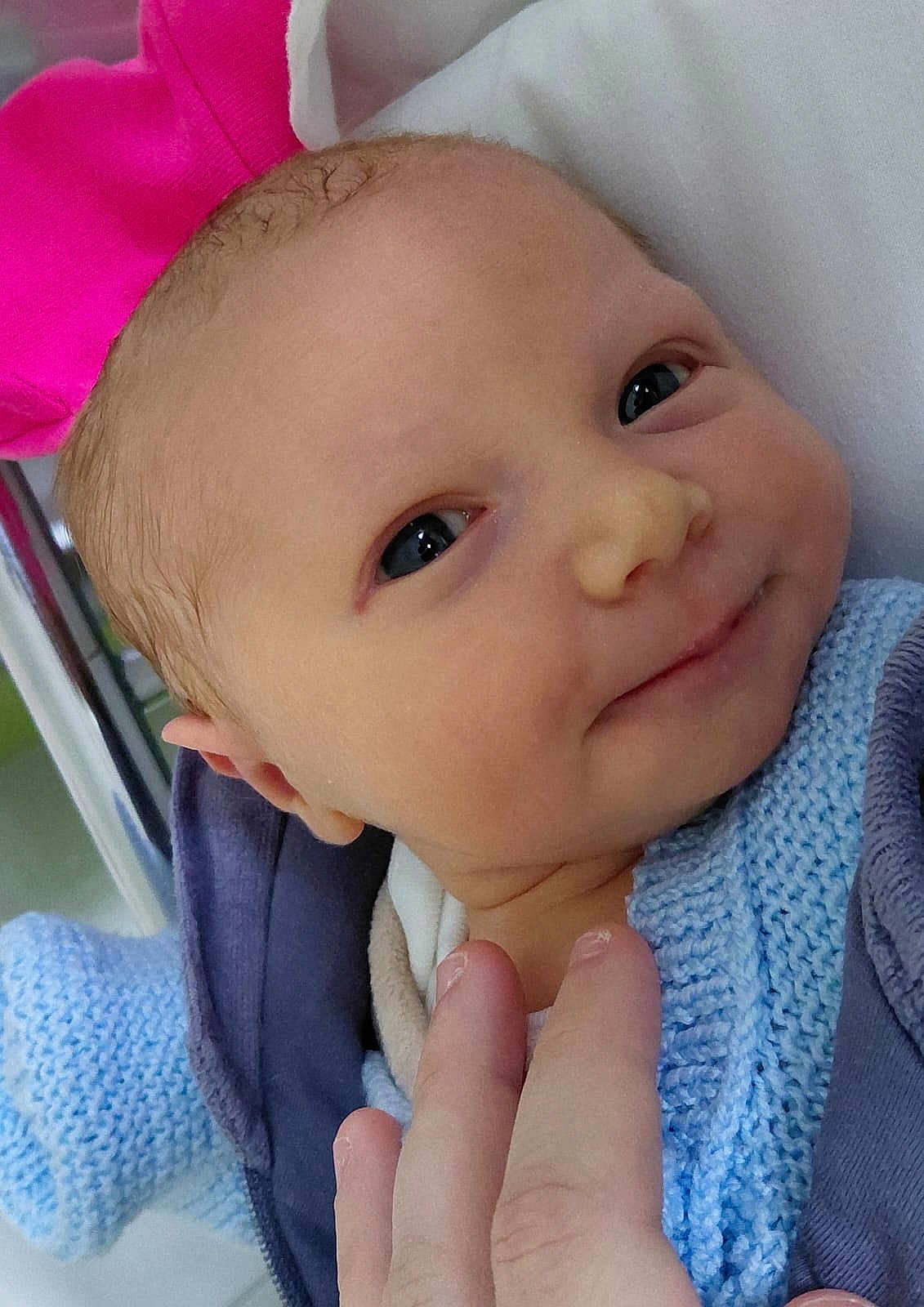 Elena participe au concours pour gagner de l'argent avec cette photo : baby, newborn, infant, face, eyes, smile, hand, fingers, blanket, knit_sweater, pink_hat, blue_clothing, cheek, skin, portrait, close_up, hospital_bassinet, metal_rail, caregiver_hand, adorable