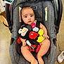 baby, car_seat, plush_toy, mickey_mouse, indoor, child, infant, toy, footwear, floor, straps, seat, pink_clothing, red, yellow, black, white, curious, sitting, childcare