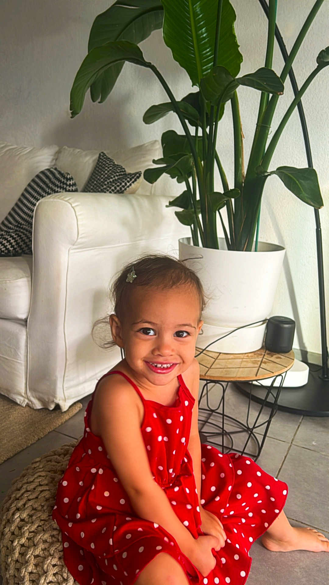 Lyah a rejoint le concours — aidez-le/la à gagner de superbes lots ! child, girl, red_dress, polka_dot, smile, hair_clip, sitting, pouf, knitted, couch, pillows, plant, indoor, floor, table, pot, happy, cute, home, decor