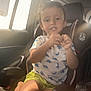 car_interior, car_seat, casual_clothing, child, cute, daylight, dinosaur_shirt, hand, indoor, kid, person, portrait, seat, seatbelt, shorts, smiling, sunlight, travel, window, young_child
