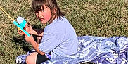 Zoey-Ann is registered to the contest to win money with this photo: blanket, casual, child, childhood, daylight, fishing_rod, fun, girl, grass, leisure, nature, outdoor, play, portrait, purple_bow, recreation, shorts, sitting, toy, tshirt