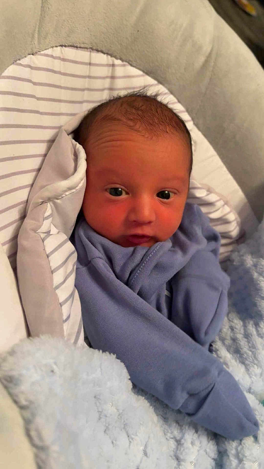 Brodie is registered to the contest to win money with this photo: baby, infant, blue_clothing, blanket, pillow, bed, face, eyes, newborn, cozy, soft, sleeping_area, cute, child, portrait, indoors, small, head, wrapped, resting