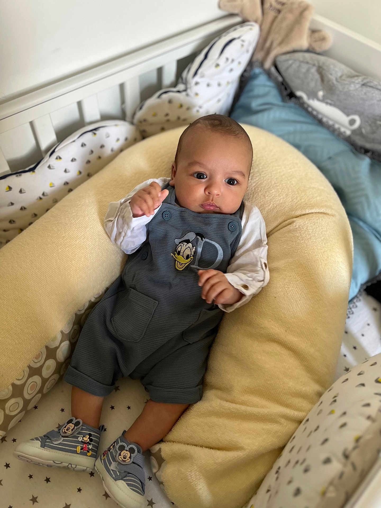 Mohamed Oussaid a rejoint le concours — aidez-le/la à gagner de superbes lots ! baby, infant, crib, baby_nest, cushion, clothing, donald_duck, mickey_mouse, footwear, sneakers, person, indoors, cute, child, comfortable, resting, soft, patterned_bedding, white_wall, cute_outfit